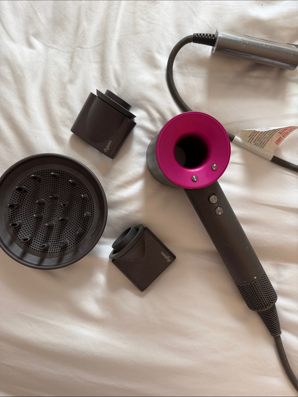 Dyson hair dryer in magenta and matte gray with attachments